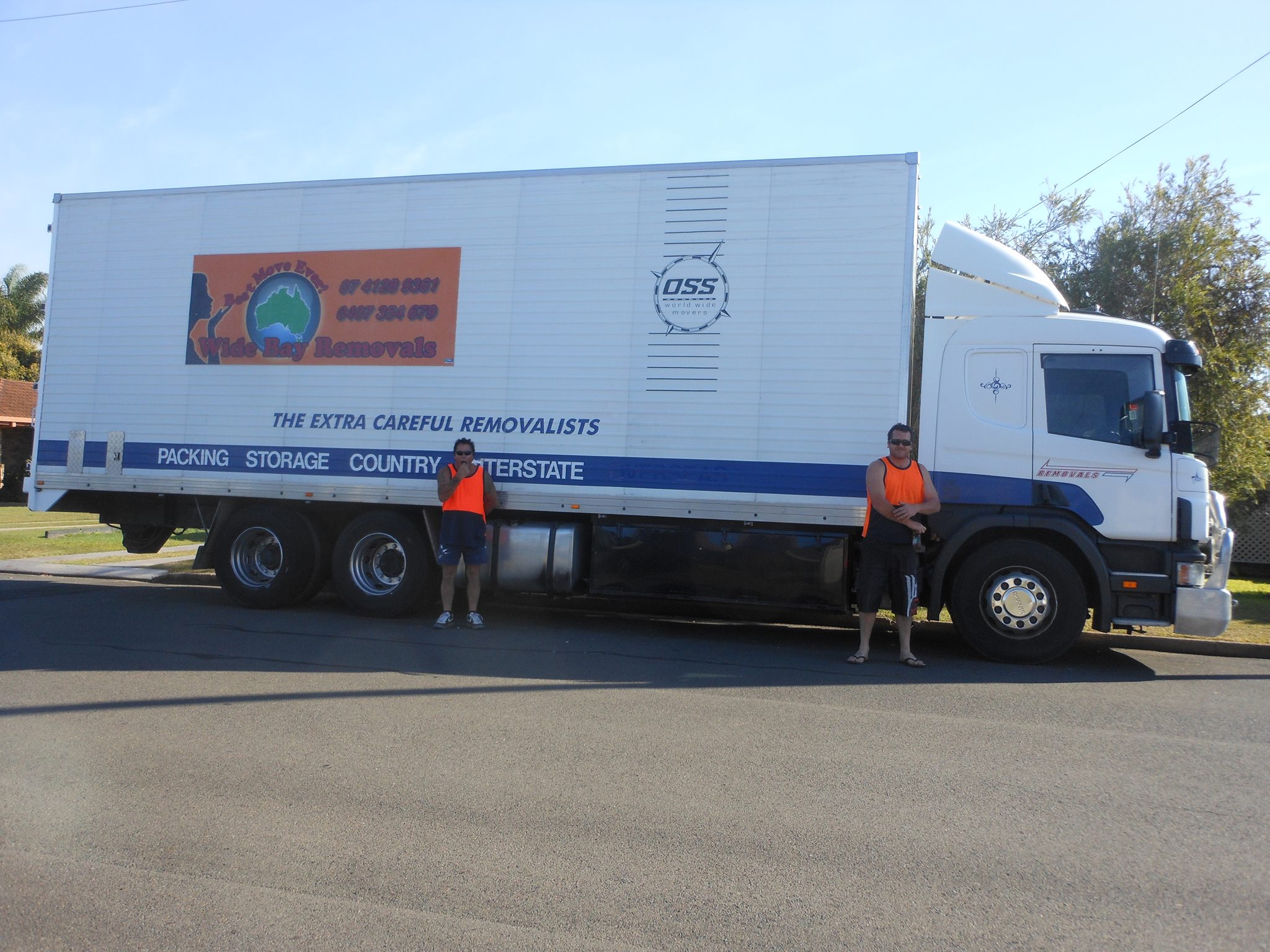 Two removalists in hi-vis beside a signwritten removals truck on a street