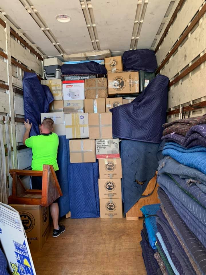 Removalist in a hi-vis shirt stacking boxes and blanket-wrapped furniture in a truck