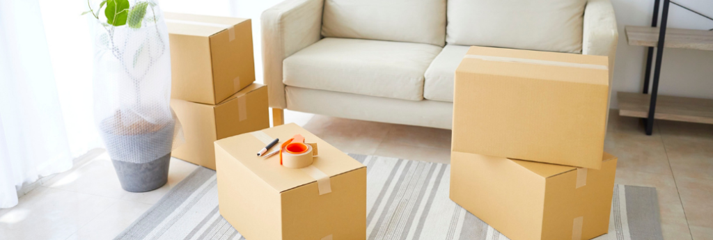 Taped moving boxes in a living room beside a cream sofa