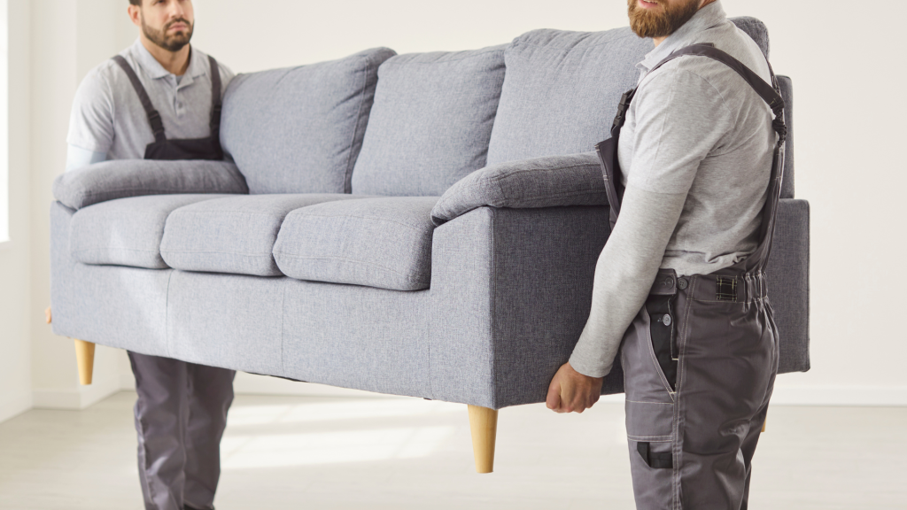 Two removalists in overalls carrying a grey sofa