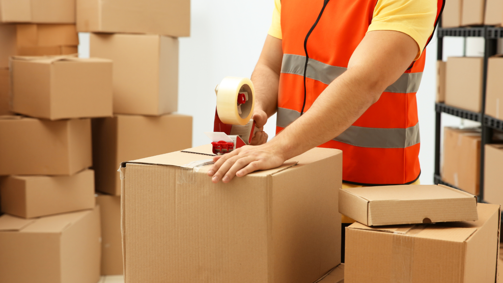Worker in a hi-vis vest taping up a cardboard box among stacked cartons