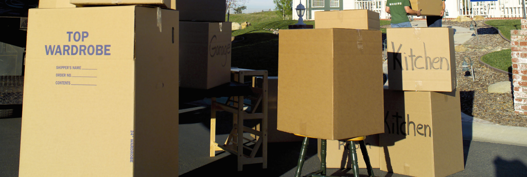 Packed moving boxes labelled Top Wardrobe and Kitchen on a driveway